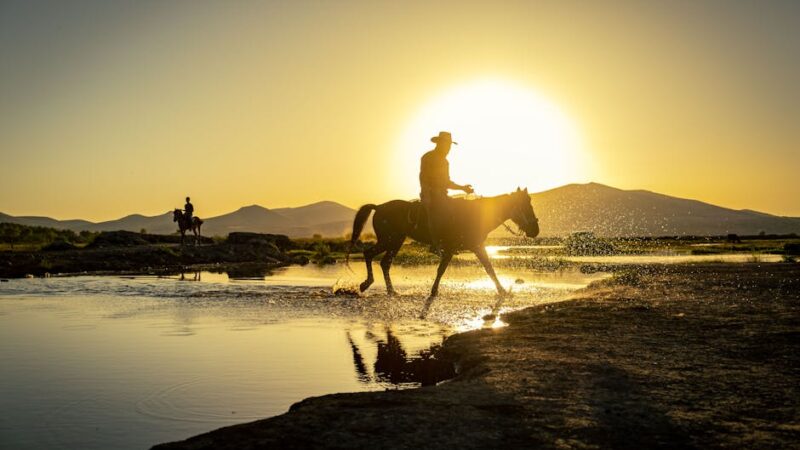 Two horseback riders with dramatic silhouettes against a stunning sunset backdrop.