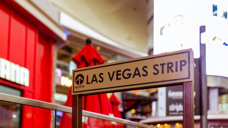 Iconic Las Vegas Strip sign with vibrant city life background.